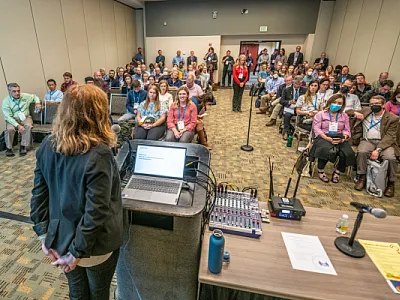 A woman presents research in a crowded room.