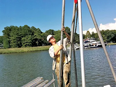 Barret Wessel looks up at a successful soil core sample from his graduate work on Chesapeake Bay. This one contained about three meters of soil, pulled up through the deck hatch open near Wessel’s feet. Photo courtesy of Barret Wessel.