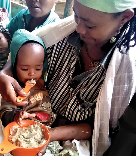A caregiver in southern Ethiopia feeds a toddler using the Healthy Baby Toolkitâa bowl and slotted spoon that indicate how much and what texture porridge to feed young children. Photo by A. Frezer.